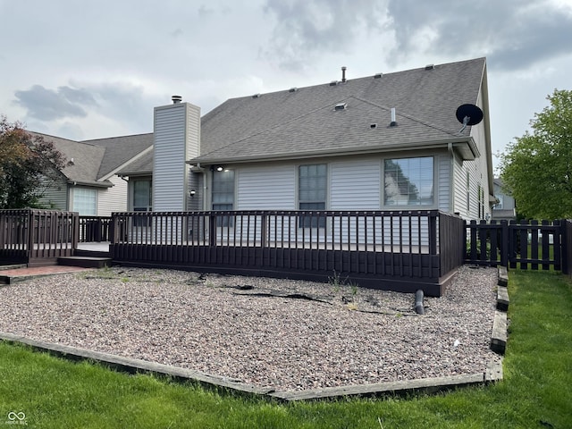 back of property with a deck, roof with shingles, and fence