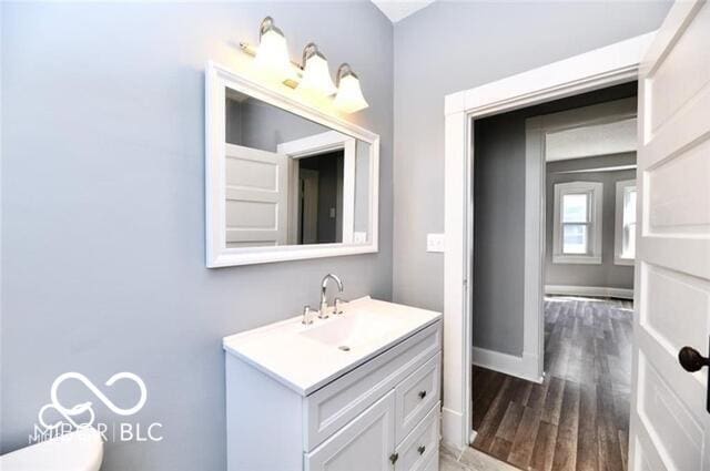half bathroom with wood finished floors, vanity, toilet, and baseboards