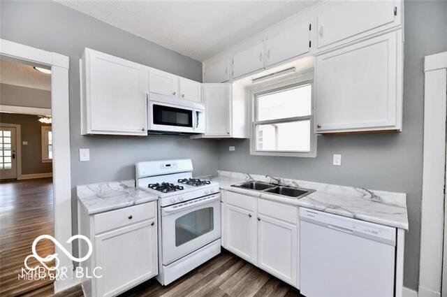 kitchen with white appliances, a sink, dark wood-style flooring, and white cabinets