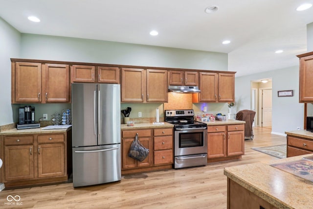 kitchen with appliances with stainless steel finishes, under cabinet range hood, brown cabinets, light countertops, and light wood-style floors