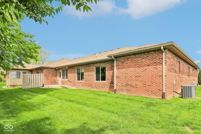 back of house featuring central AC unit, brick siding, and a yard