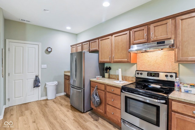 kitchen featuring stainless steel appliances, under cabinet range hood, brown cabinetry, light wood-style flooring, and recessed lighting