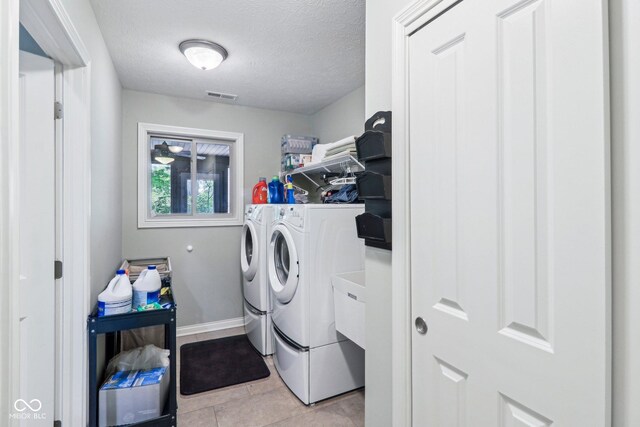 clothes washing area featuring washing machine and dryer, baseboards, a textured ceiling, and light tile patterned flooring