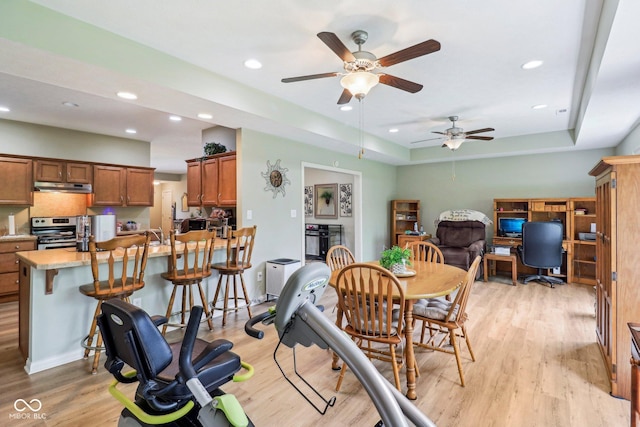 dining space featuring light wood-style floors, a desk, ceiling fan, recessed lighting, and a tray ceiling