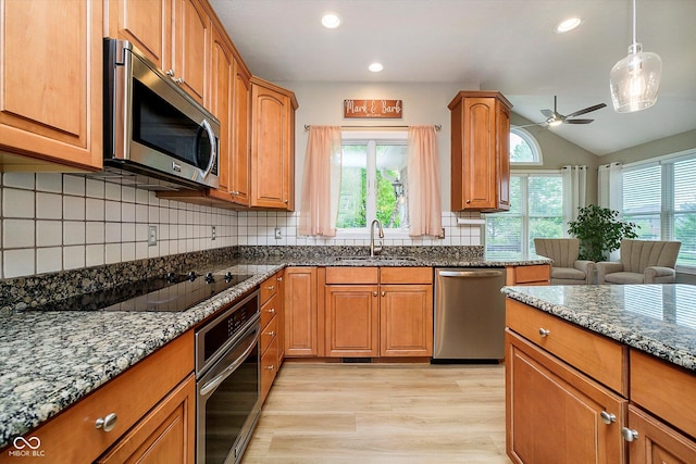 kitchen with appliances with stainless steel finishes, a sink, light wood-style floors, dark stone countertops, and a ceiling fan