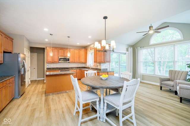 dining room featuring light wood-type flooring, ceiling fan, a chandelier, baseboards, and vaulted ceiling