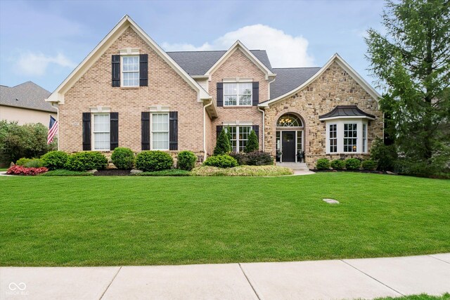 view of front facade with stone siding, a front yard, and brick siding