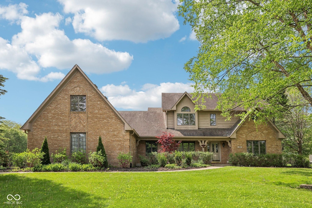 view of front facade with brick siding, a front yard, and a shingled roof