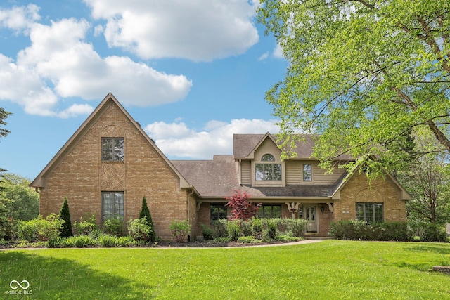 view of front facade with brick siding, a front yard, and a shingled roof