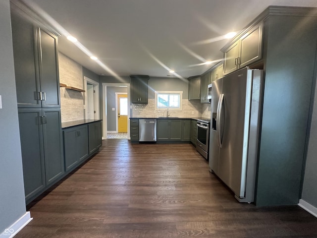 kitchen with appliances with stainless steel finishes, a sink, dark wood finished floors, tasteful backsplash, and baseboards