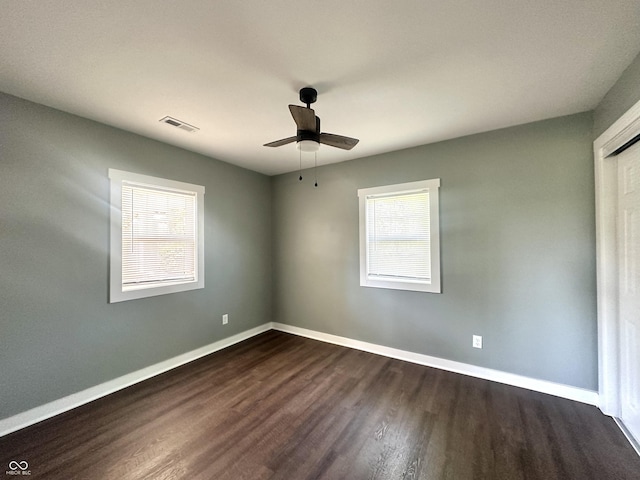 empty room with dark wood-type flooring, healthy amount of natural light, ceiling fan, and baseboards