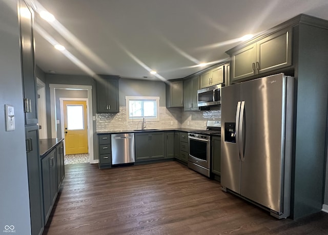 kitchen with stainless steel appliances, dark wood-type flooring, dark countertops, and tasteful backsplash