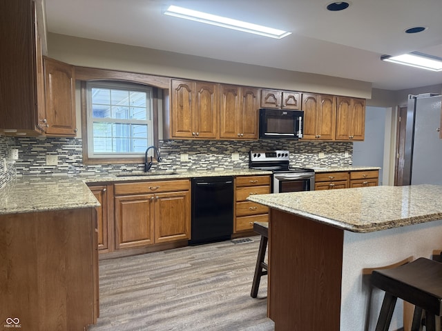 kitchen featuring black appliances, a sink, a kitchen bar, light wood-style floors, and tasteful backsplash