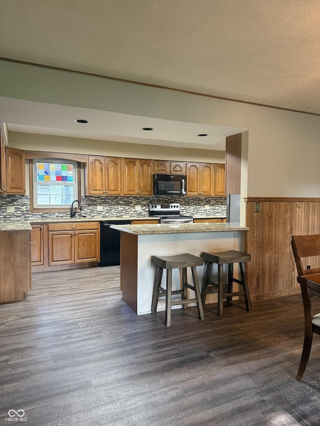 kitchen with black appliances, brown cabinets, wood finished floors, a wainscoted wall, and backsplash