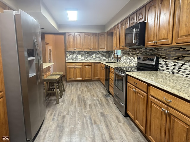 kitchen with black appliances, a sink, light wood-style floors, and brown cabinets