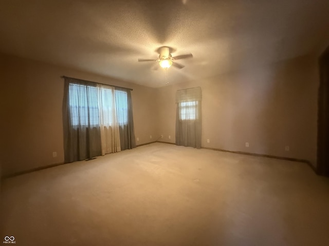 empty room with a ceiling fan, baseboards, light colored carpet, and a textured ceiling