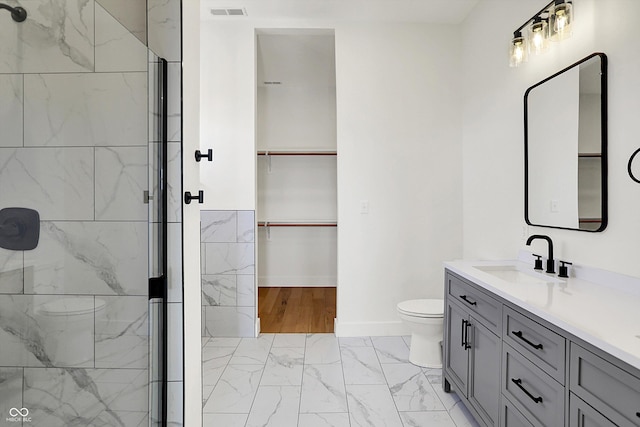 bathroom featuring marble finish flooring, toilet, a shower stall, vanity, and a spacious closet