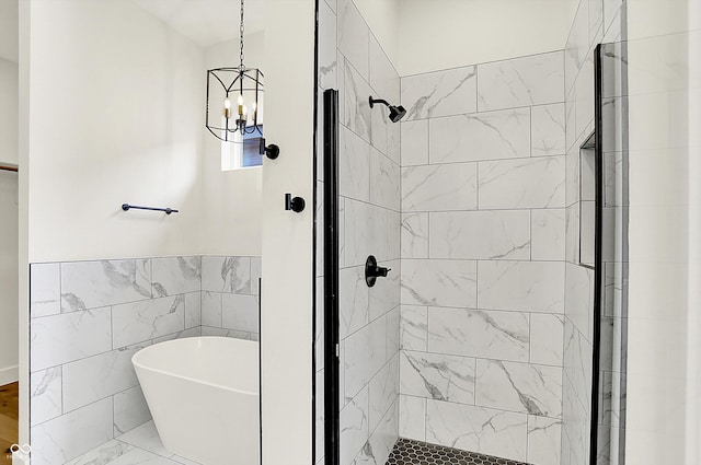 full bathroom featuring a chandelier, a stall shower, a freestanding bath, marble finish flooring, and tile walls