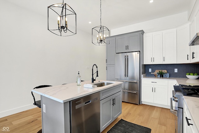kitchen featuring high end appliances, a sink, a chandelier, light wood-type flooring, and hanging light fixtures