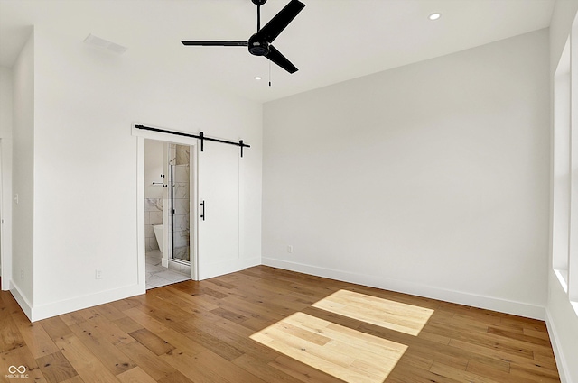 unfurnished bedroom with hardwood / wood-style floors, a barn door, baseboards, recessed lighting, and connected bathroom