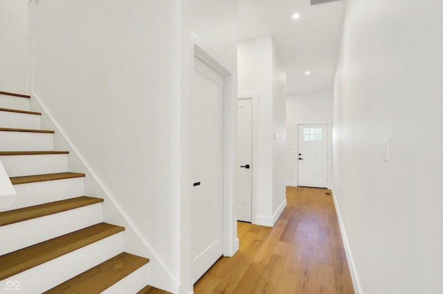hall featuring baseboards, stairs, light wood-style floors, and recessed lighting