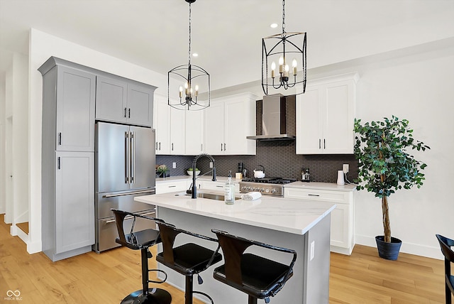 kitchen featuring high quality fridge, wall chimney range hood, a chandelier, decorative backsplash, and light wood-style flooring