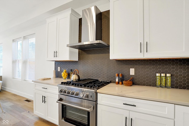 kitchen with high end range, wall chimney exhaust hood, light wood-style flooring, and decorative backsplash