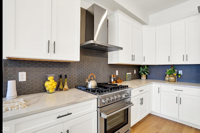 kitchen with high end stainless steel range, wall chimney exhaust hood, white cabinetry, light wood-style flooring, and decorative backsplash