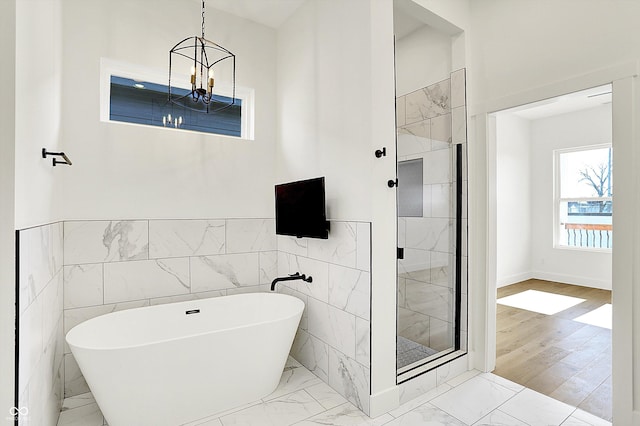 bathroom featuring marble look tiles, a chandelier, a freestanding tub, a shower stall, and a wainscoted wall