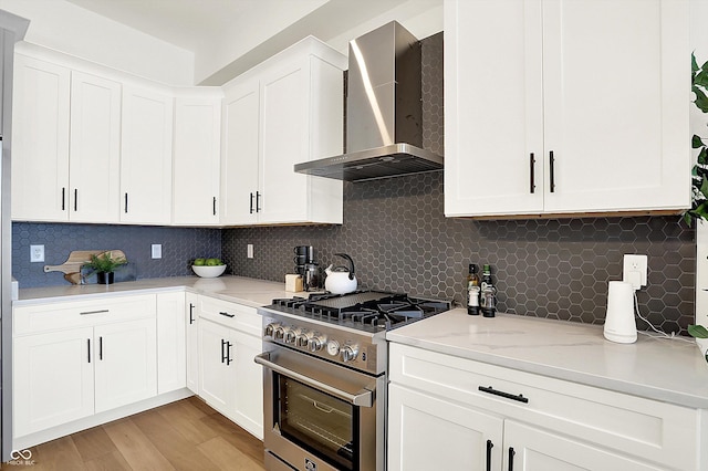 kitchen with stainless steel range, wall chimney exhaust hood, white cabinets, and backsplash
