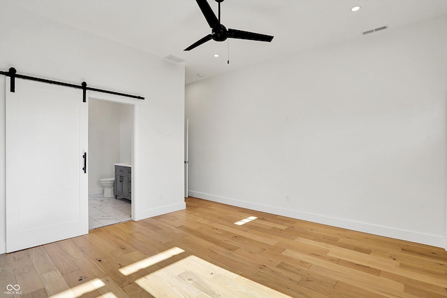 unfurnished bedroom featuring a barn door, light wood finished floors, baseboards, connected bathroom, and recessed lighting