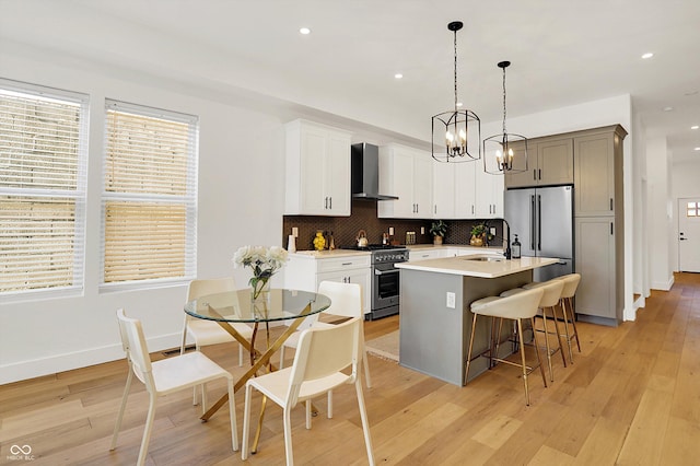 kitchen with high end appliances, wall chimney exhaust hood, a sink, a kitchen bar, and a chandelier