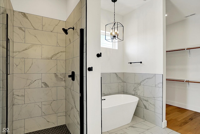 full bathroom with a stall shower, a chandelier, a freestanding bath, a walk in closet, and marble finish floors