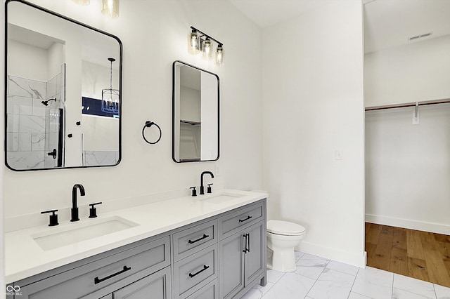 full bathroom featuring baseboards, toilet, a spacious closet, a tile shower, and double vanity