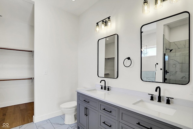 bathroom with toilet, a shower stall, baseboards, double vanity, and a walk in closet