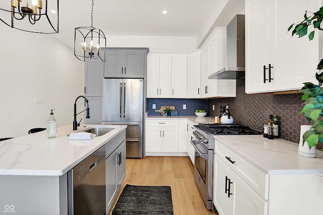 kitchen with high end appliances, wall chimney exhaust hood, a sink, a chandelier, and recessed lighting