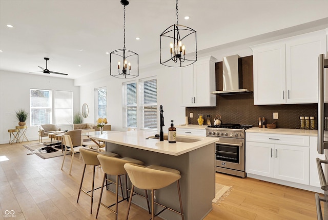 kitchen featuring high end range, wall chimney exhaust hood, a chandelier, light wood finished floors, and recessed lighting