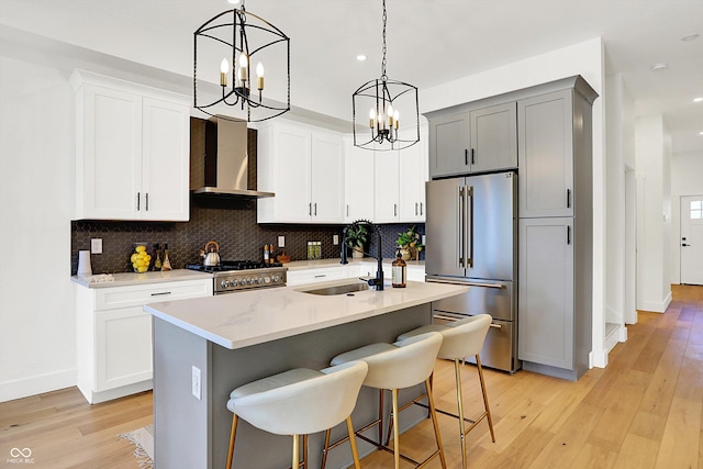 kitchen featuring a sink, high end fridge, wall chimney range hood, a chandelier, and recessed lighting