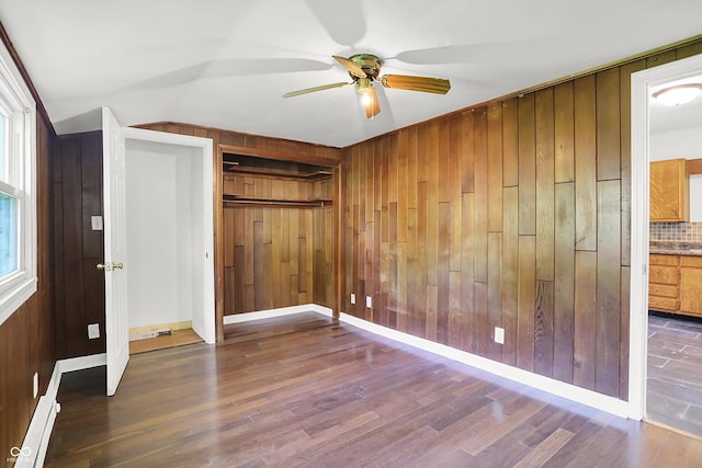 unfurnished bedroom featuring wood walls, wood finished floors, a closet, baseboards, and ceiling fan