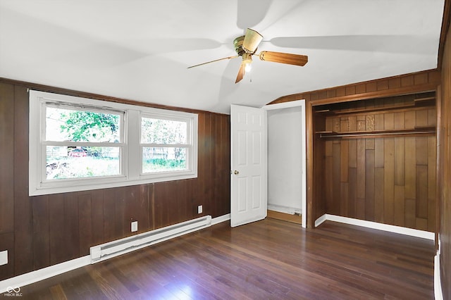 unfurnished bedroom with baseboard heating, lofted ceiling, dark wood-type flooring, wood walls, and a closet