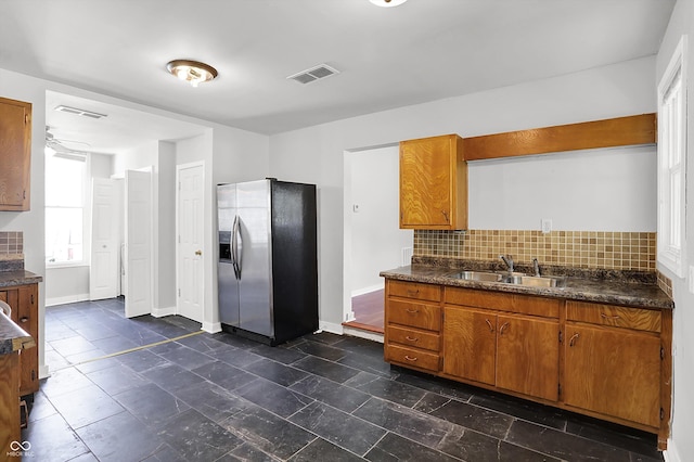 kitchen featuring stainless steel fridge with ice dispenser, a sink, dark countertops, and brown cabinetry
