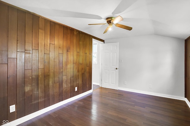 unfurnished room featuring ceiling fan, wood finished floors, baseboards, wooden walls, and vaulted ceiling