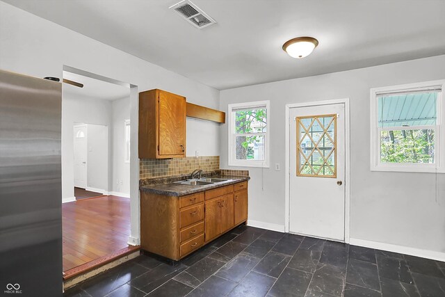 kitchen with a sink, brown cabinetry, dark countertops, baseboards, and tasteful backsplash
