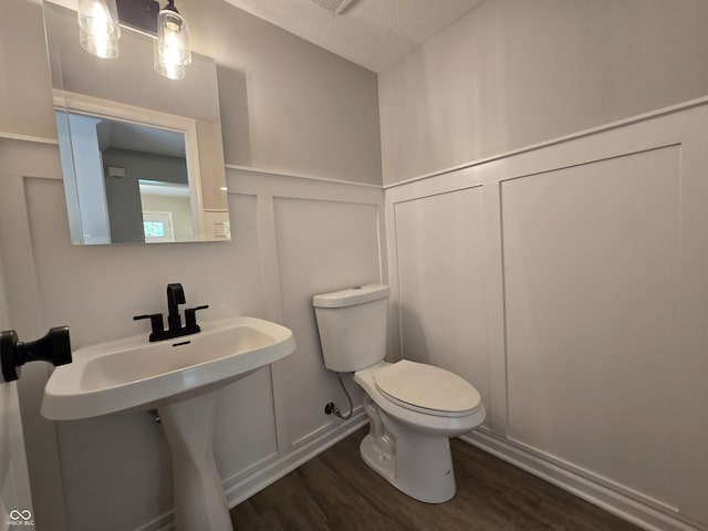 6369 Kelsey Dr, Indianapolis, IN 46268 - half bathroom featuring a decorative wall, toilet, wood finished floors, a wainscoted wall, and a sink