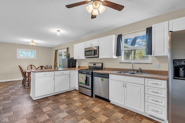 kitchen with a sink, appliances with stainless steel finishes, a peninsula, white cabinetry, and a ceiling fan