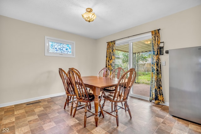 dining area with baseboards, healthy amount of natural light, stone finish floors, and a textured ceiling