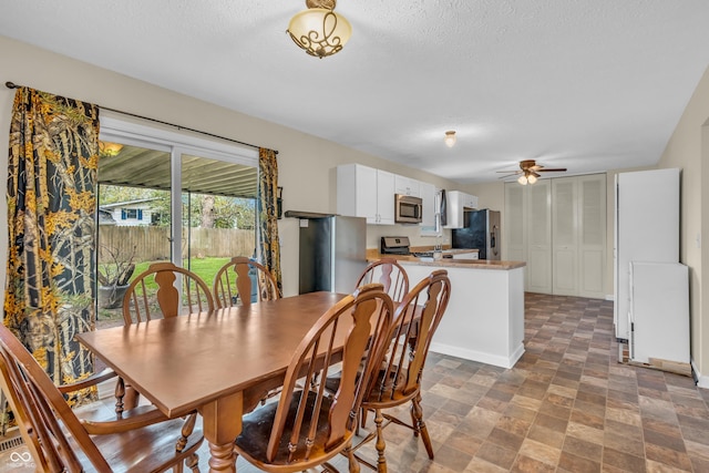 dining area with a ceiling fan, stone finish flooring, and a textured ceiling