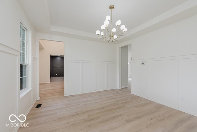 unfurnished dining area with a decorative wall, a chandelier, light wood-style floors, a tray ceiling, and healthy amount of natural light