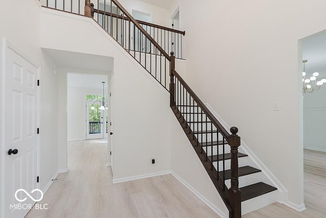 staircase featuring a chandelier, wood finished floors, baseboards, and a towering ceiling