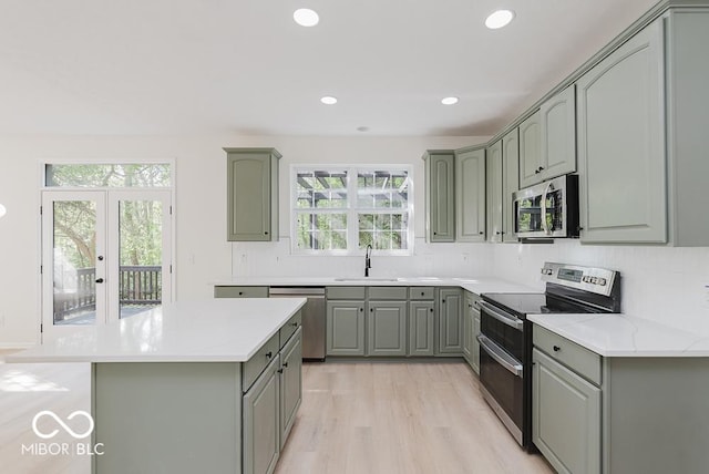 kitchen featuring appliances with stainless steel finishes, gray cabinets, a sink, light wood-type flooring, and backsplash
